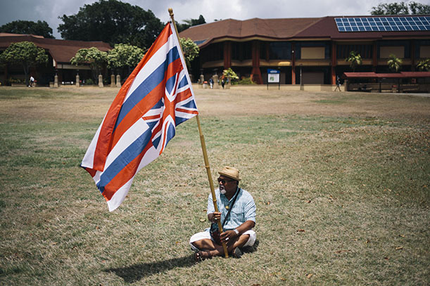 HONOLULU, HAWAII - APRIL 13:  A protestor sits on the Great Lawn with a Hawaiian Flag during a protest of the Thirty Meter Telescope in front of the Great Lawn at Kapiolani Community College on April 13, 2015 in Honolulu, Hawaii.