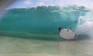 A surfer does a bottom turn on the edge of his bodyboard to make it under the lip on a heavy wave at sandy beach.